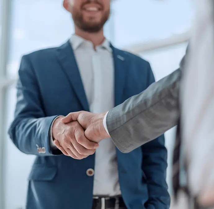 Two men in business suits shaking hands in an office setting.